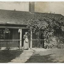Woman looking out into the distance, standing in front of house on porch